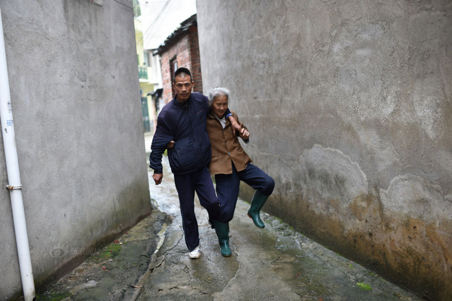 Huang Huiying helps her mentally-retarded son walk in the village. Huang&apos;s two sons also suffer from muscular atrophy which makes them unable to control their bodies&apos; balance and even unable to walk. [Photo/Sina]