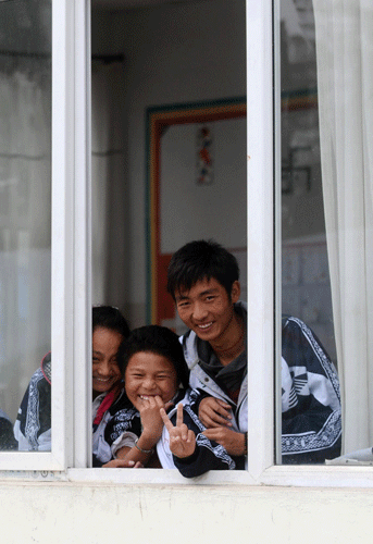 Three students smile inside the window, looking at the lens of the camera. 