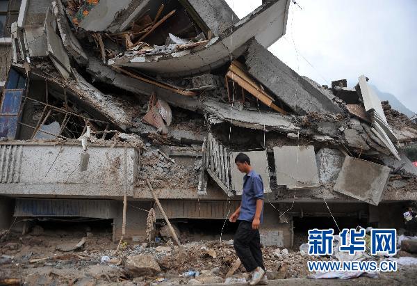 8月13日，一位受灾群众走过被泥石流冲毁的房屋。