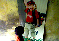 一个穷人家的小男孩站在一块广告牌前，广告里和他年龄相仿的男孩在喝一种健康美味的饮料，小男孩却买不起。