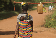 一位年轻的妈妈从农场归来，背着孩子，头上顶着锄头和水桶。