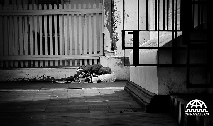 一位老妇躺在街上，等待路人的施舍。她没有家，就睡在街边。