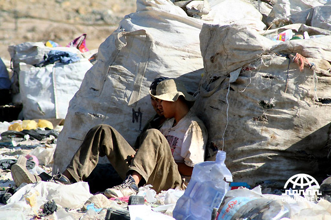 两个男子靠着垃圾堆睡着了。很多家庭住在垃圾场，靠捡垃圾为生。
