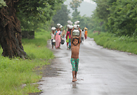 一个八九岁的小女孩头上顶着一大桶水走在回家的路上，她每天都要这样走大约三公里的路程。