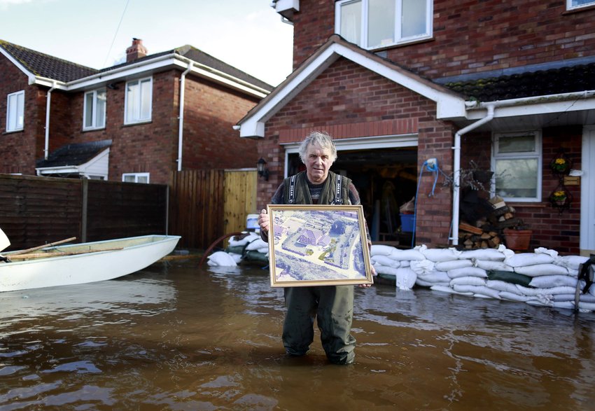 当地时间2014年2月14日，英国Moorland，64岁的建筑师Derek Bristow手持一张照片站在屋外洪水中。他表示这张照片是其在洪水来袭时，将最先拯救的物品。
