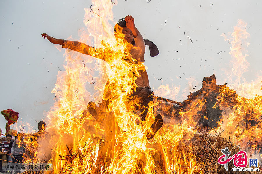  炮竹三响过后，长者点燃熊熊篝火，游行队伍依次从火墩上跃身而过，先是清道旗、标旗、宫灯、锣鼓等，然后是“老爷”坐的八抬大轿，接着村民们跟着一一跃过火墩。中国网图片库 邓飞/摄