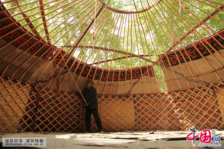  挂第二层白毡时需要三个人，里面一人用光棍子顶，碗面两人用力拉绳子，因为毡房顶不是弧形的，因此白毡就会在左右两人的拉扯下，挂上去。中国网图片库 孙继虎/摄