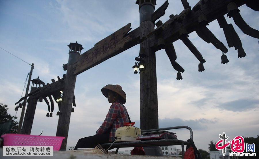  2015年6月5日，海南琼海市潭门镇一名渔民坐在沧桑千百年的渔港码头出售渔货。千百年来，海南渔民传抄《更路簿》，图中记载的航海路线，航行要领，气象水流，更不知是多少渔民用鲜血换来的“生命航线”。中国网图片库 蒙钟德 摄