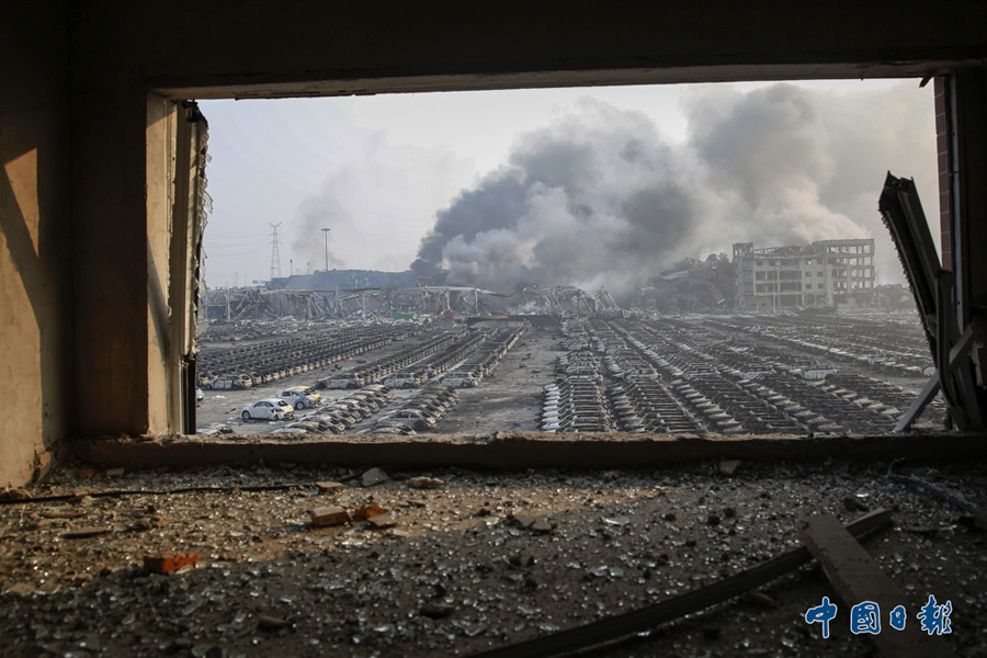 2015年8月13日，天津危险品仓库爆炸现场，透过一处被损毁的窗户可见一片狼藉的新车停车场。8月12日晚，天津港国际物流中心区域内瑞海公司所属危险品仓库发生爆炸，事故造成严重的人员伤亡。中国日报亚洲新闻图片网 单海汉 摄影