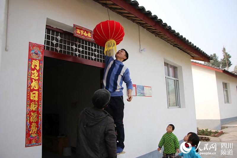 村民代杰在门前挂喜气的红灯笼，脸上洋溢着幸福的笑容。（张枥 摄）