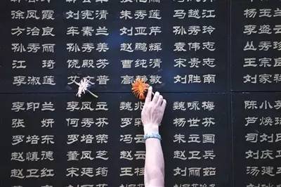  ▲7月28日，一名唐山市民将鲜花粘附在遇难亲人的名字旁。新华社记者 牟宇 摄