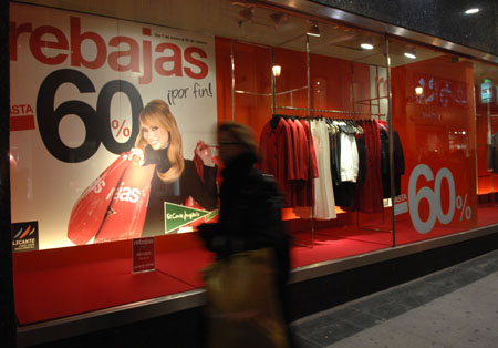 Pedestrians pass by a store window with discount signs in center of Madrid, capital of Spain on January 8, 2009. [Xinhua]