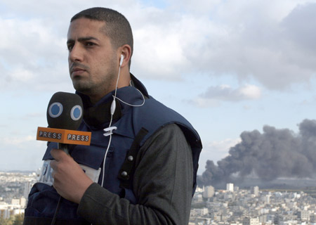 Yousef Alhelo, Press TV correspondent in Gaza, covers the latest developments in Gaza Strip from the roof of a building in Gaza while a smoke rises behind him, on Jan. 9, 2009. An Israeli air strike hits a roof of Aljawhra tower in Gaza on Friday, causing one injury among journalists.