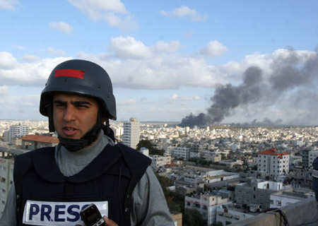 Tamer Almisshal, Al-jazeera correspondent in Gaza, covers the latest developments in Gaza Strip from the roof of a building in Gaza while a smoke rises behind him, on Jan. 9, 2009. 