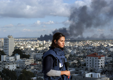 Shirn Tadros, Aljazeera International correspondent in Gaza, covers the latest developments in Gaza Strip from the roof of a building in Gaza while a smoke rises behind him, on Jan. 9, 2009. 