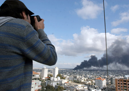 Wissam Nassar, Xinhua photographer correspondent in Gaza, covers the latest developments in Gaza Strip from the roof of a building in Gaza while a smoke rises behind him, on Jan. 9, 2009.