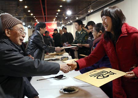 Liu Jiangshu (L), professor of China Academy of Art, presents his work of 'fu', meaning 'good wishes', to a woman during a calligraphy activity held in Hangzhou, capital of east China's Zhejiang Province, on January 15, 2009, to greet the Chinese lunar New Year starting from January 26.