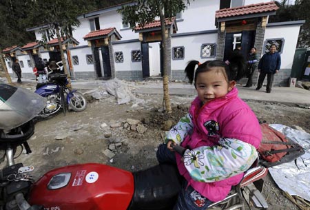 5-year-old girl Wei Zhuoyue sits on a motorcycle in front of new houses at Qipan village in Xiang'e town of Dujiangyan City, southwest China's Sichuan Province, on January 21, 2009. 