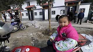 5-year-old girl Wei Zhuoyue sits on a motorcycle in front of new houses at Qipan village in Xiang'e town of Dujiangyan City, southwest China's Sichuan Province, on January 21, 2009.