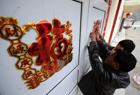 Song Zhongsheng and his daughter Song Yuxia paste Chinese character stickers wishing good luck on the doors at Songba village in Wenxian County of Longnan City, northwest China's Gansu Province, on January 23, 2009. A total of 66 quake-affected families at Songba village moved into 216 new houses before the Chinese Lunar New Year.