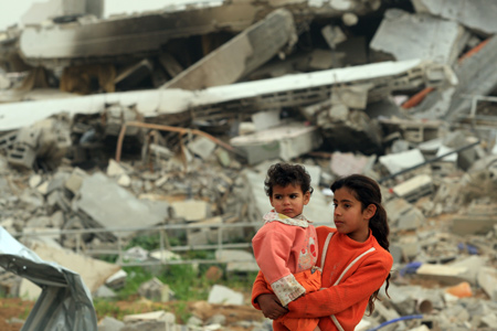 A Palestinian girl holding a child stand before buildings destroyed in Israeli military operations in Zitton, southern Gaza City, on January 24, 2009. A large number of houses were destroyed in the conflict in Gaza Strip. [Xinhua]