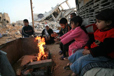 Palestinians get warm by a fire in the rubbles in al Moghraqa area in the central Gaza Strip, on January 29, 2009. The reconstruction of Gaza Strip after a ceasefire is almost at a standstill due to the continuous blockage of Gaza by Israel and different opinions on receiving international aid in the Palestinian side.