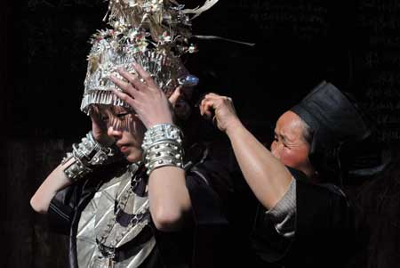 A girl of Miao ethnic group puts on her headwear with the help of an old woman in the Zhanliu Village of Jianhe County, southwest China's Guizhou Province, on January 31, 2009.