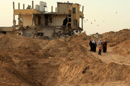 Palestinians walk past a destroyed house at a refugee camp in Jabalia, northern Gaza Strip, on January 31, 2009.