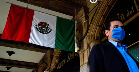 A man wearing a mask walks past a Mexican flag in Mexico City, capital of Mexico, on April 24, 2009. The government of Mexico City is launching a massive vaccination campaign throughout the city against swine flu, which has possibly killed dozens nationwide. 