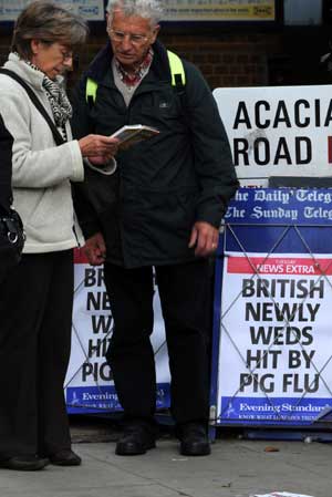 People stand beside placards of swine flu news at a newsstand in London, the United Kingdom, on April 28, 2009. 