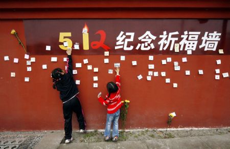 Two kids stick cards written with their best wishes to the kids in the earthquake-hit areas to a memorial wall in Suining, southwest China's Sichuan Province, April 4, 2009, the day of Chinese Qingming Festival or Tomb-sweeping Day. The 18-meter long and 3-meter high memorial wall was set up here for people to express condolences to victims in the devastating earthquake striking Sichuan Province on May 12, 2008. (Xinhua/Zhong Min)