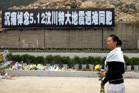 A women holding a flower walks past a banner that reads "Deep Condolence on 5.12 Wenchuan Quake Compatriots" in site of former Beichuan County Town, southwest China