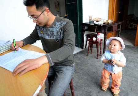 Li Yongbing examinies his students' homework while his son Li Zihao playing beside at home in Fuxin Township, Mianzhu City, Sichuan Province, southwest China, on May 1, 2009. Li Yongbing, 28 years of age, is a teacher at a primary school at Qingping Village in Mianzhu City. His wife Wang Qin, who was also his colleague, died in the May 12 earthquake last year and left their little son behind. In the first few months after the disaster, Li Yongbing worked as a volunteer.