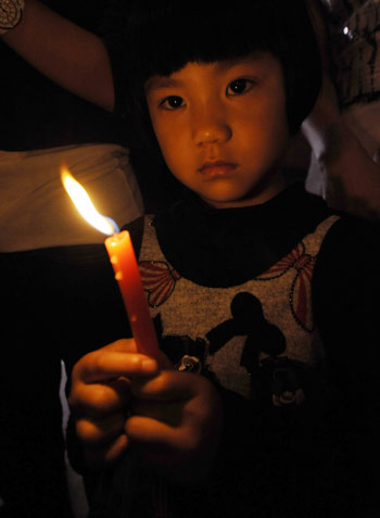 A child holds a candle during an activity to commemorate the victims of the fatal May 12, 2008 Wenchuan earthquake, in Zhengzhou, capital of central China's Henan Province, on May 12, 2009. 
