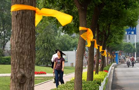 Pedestrians walk past trees tied with yellow ribbons on a street in north China's Tianjin, on May 12, 2009. Volunteers tied thousands of yellow ribbons on buses, buildings and trees as a way to commemorate the victims of the May 12, 2008 Wenchuan earthquake.