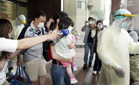 A family, who were on the same plane as the man confirmed of A/H1N1 influenza, are led by a quarantine worker at a hospital in Taipei, southeast China's Taiwan, on May 20, 2009.