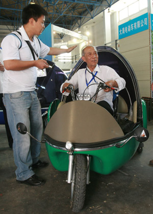 A working staff shows a visitor how to drive a mini three-wheel vehicle driven with electric power at the 12th Beijing International Science and Technology Exposition held in Beijing, on May 20, 2009.