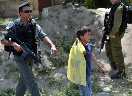 Photo taken on May 18, 2009 shows a Palestinian boy walking by armed Israeli soldiers in the West Bank city of Hebron.