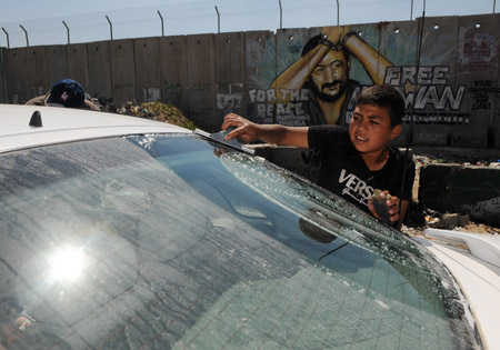 Photo taken on May 28, 2009 shows a Palestinian boy cleaning a window of a car passing by the separation wall in the west bank city of Ramallah.