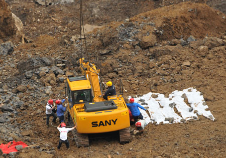 Workers help unload the excavator from a MI-26 helicopter at the landslide site in Wulong County, southwest China's Chongqing Municipality, on June 11, 2009.