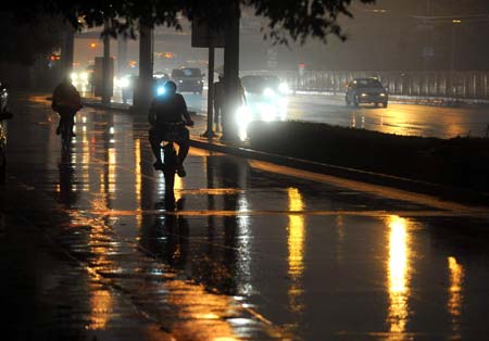 Local residents ride in heavy rain as the street lamps are turned on in downtown Beijing, China, on June 16, 2009. Local authority released a yellow alert for lightings on Tuesday.