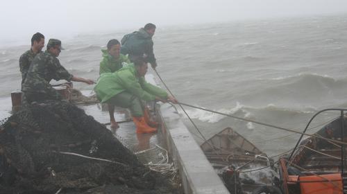 Soldiers and fishermen strive to fasten a fishing boat amid stormy weather in Zhangzhou, east China's Fujian Province on Sunday, June 21, 2009. The provincial meteorological bureau issued an orange alert for torrential rains on Monday, after tropical storm Linfa arrived on Sunday. 