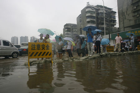 Local people wait to walk past a flooded street in Wuhan, capital city of central China's Hubei Province, June 30, 2009. The city has been hit by seasonal summer rainfalls for days.