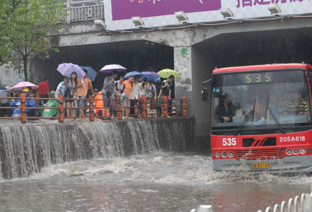 Local people look on as a city bus drives in deep rainwater on a flooded street in Wuhan, capital city of central China&apos;s Hubei Province, on June 30, 2009. The city has been hit by seasonal summer rainfalls for days.