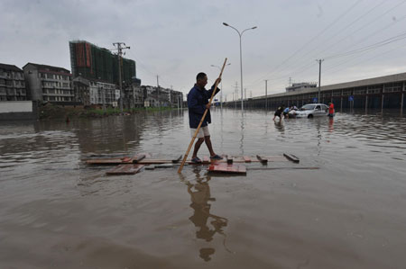 A local resident paddles a makeshift raft as others push a stranded car in deep rainwater on a flooded street in Wuhan, capital city of central China&apos;s Hubei Province, on June 30, 2009. The city has been hit by seasonal summer rainfalls for days. 