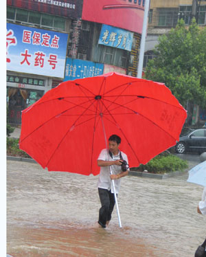 A press-photographer works in the rain on Yuanshan Avenue in Yichun City, east China's Jiangxi Province, on July 2, 2009. A storm hit Yichun City from Tuesday to Thursday. 