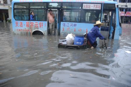 A local tricyclist struggles his way in the flood with a shut-down bus being detained nearby in downtown Yingtan City in southern China's Jiangxi Province, on July 4, 2009. Heavy rain and storm struck the city saturday paralysing part of the city's communications. 