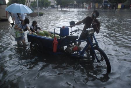 A local tricyclist struggles his way in the flood with the help of passersby in downtown Yingtan City in south China's Jiangxi Province, on July 4, 2009. Heavy rain and storm struck the city saturday paralysing part of the city's communications.