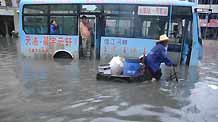 A local tricyclist struggles his way in the flood with a shut-down bus being detained nearby in downtown Yingtan City in southern China's Jiangxi Province, on July 4, 2009. Heavy rain and storm struck the city saturday paralysing part of the city's communications.