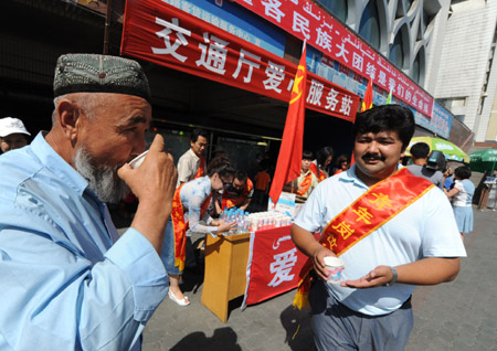 A volunteer sends a cup of water to a passenger at a passenger transport station in Urumqi, capital of northwest China's Xinjiang Uygur Autonomous Region, on July 11, 2009. Several hundred volunteers have gathered at transport stations and hospitals here to provide help since local government began to recruit volunteers on July 10.